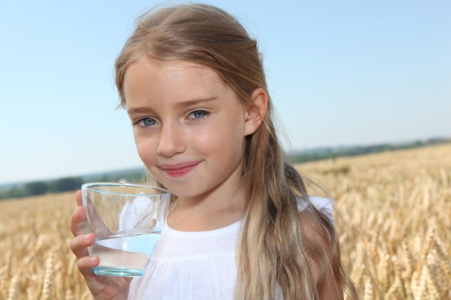 big close up little blonde girl holding a glass of water